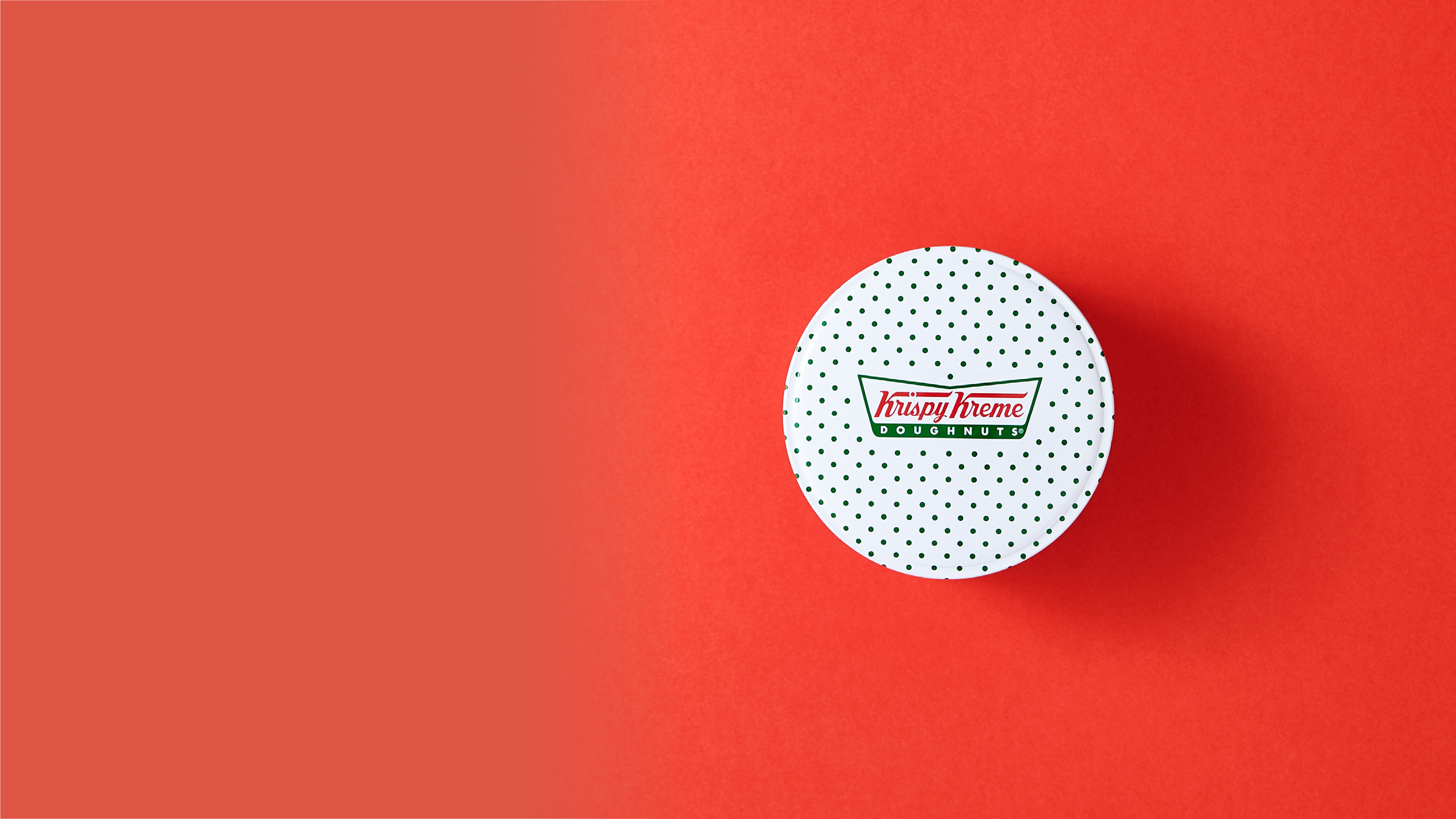 Un envase de lata de donut Krispy Kreme sobre un fondo rojo. 
