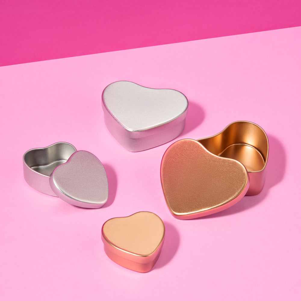 Colección de latas con forma de corazón en plata y oro rosa sobre fondo rosa.